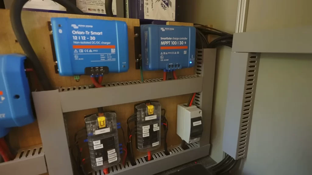 Coffre électrique du Boxer aménagé : chargeur DC-DC Victron Orion-Tr Smart 12|12-30 et régulateur solaire SmartSolar MPPT 100|30 fixés sur contreplaqué, au-dessus de deux porte-fusibles à lames étiquetés